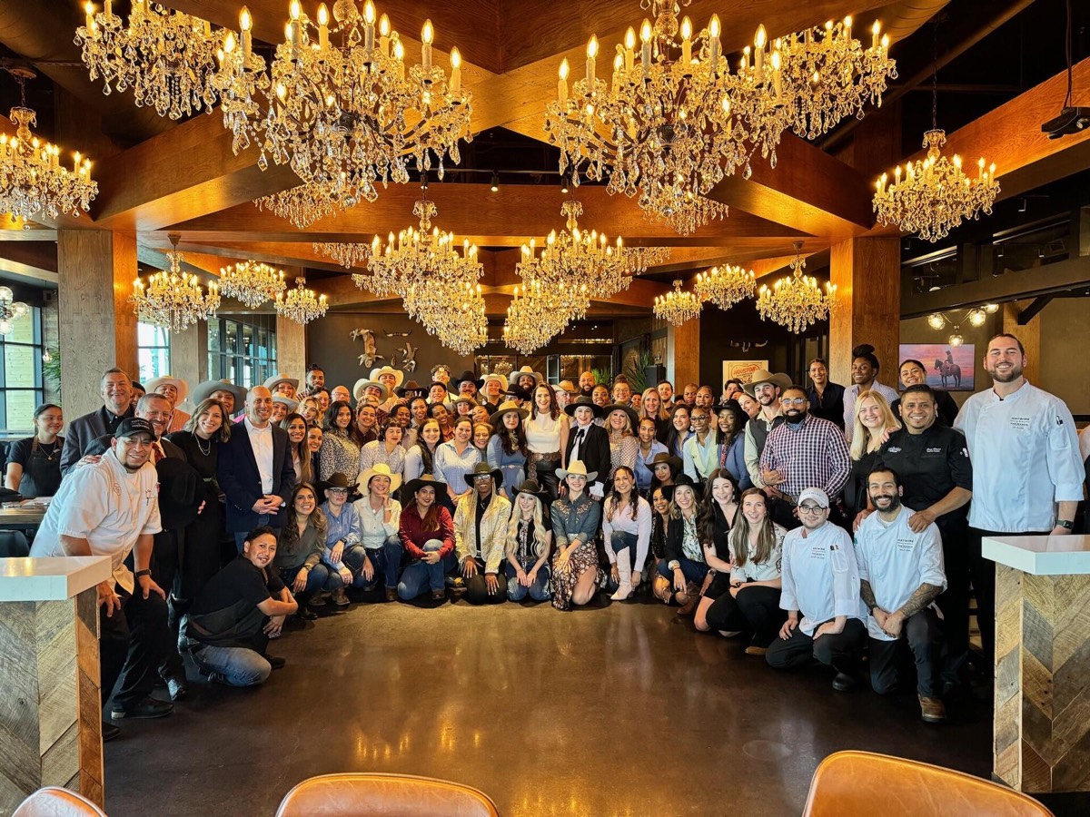 Jon Peck with the full Haywire opening team, chefs in whites, servers and leadership, gathered under crystal chandeliers in a timber-beamed dining room