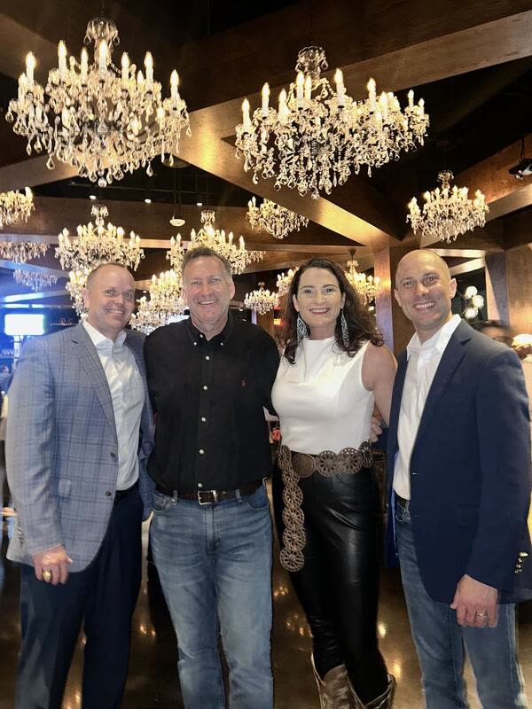 Jon Peck, in a navy blazer, with three others under crystal chandeliers in a timber-beamed dining room